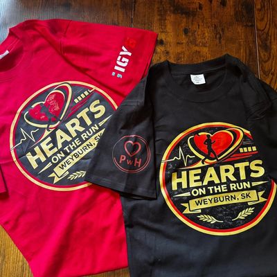 Two colorful 'Hearts on the Run Weyburn, SK' event t-shirts on a wooden surface.