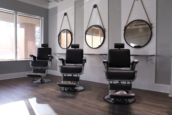 Three black barber chairs in front of circular mirrors.