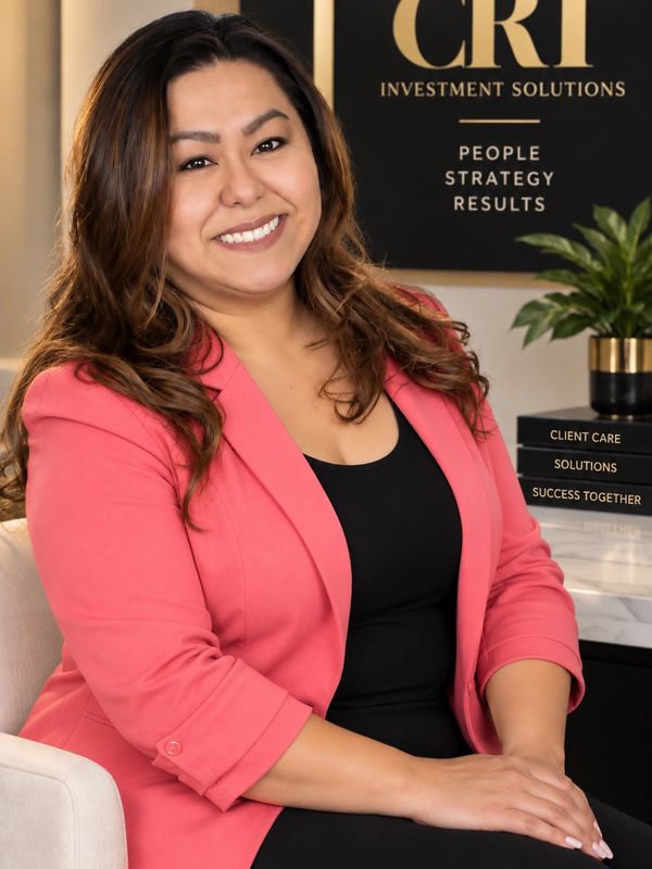 Smiling woman in pink blazer sitting with crossed hands.