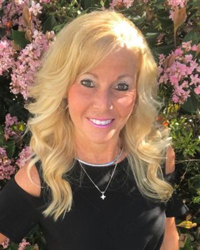 Smiling woman with blonde hair outdoors near pink flowers.