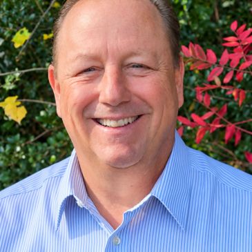 Smiling man outdoors with colorful foliage.