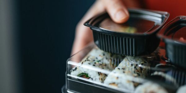 Hand holding a sushi container and soy sauce.
