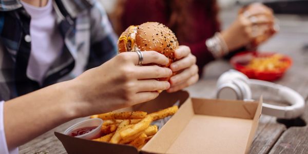Person holding a burger with fries and ketchup on table.