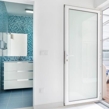 Open white door leading to blue-tiled bathroom.