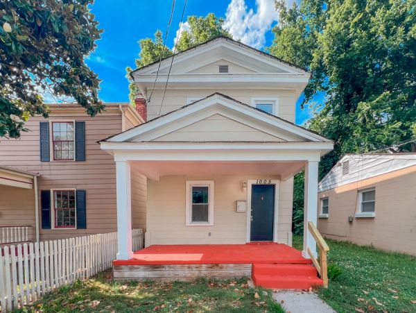 Small beige house with a bright red porch and blue door under a sunny sky.