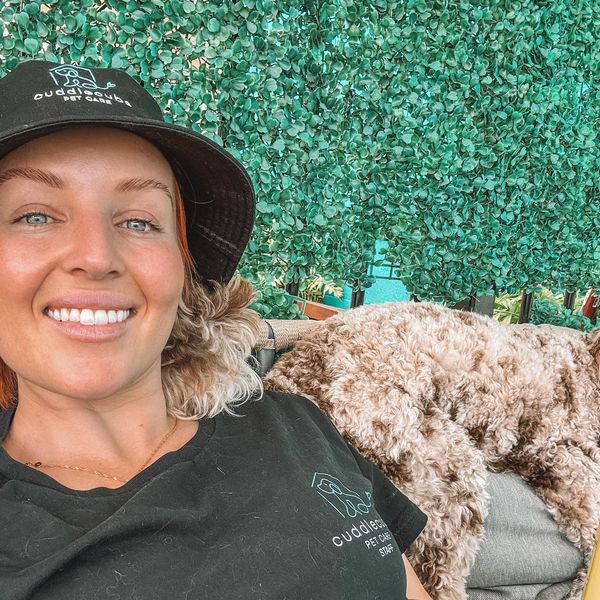Smiling woman with a curly dog resting beside her.