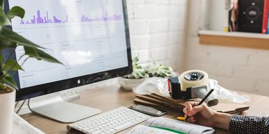 Person working at a desk with computer, notebook, and phone.