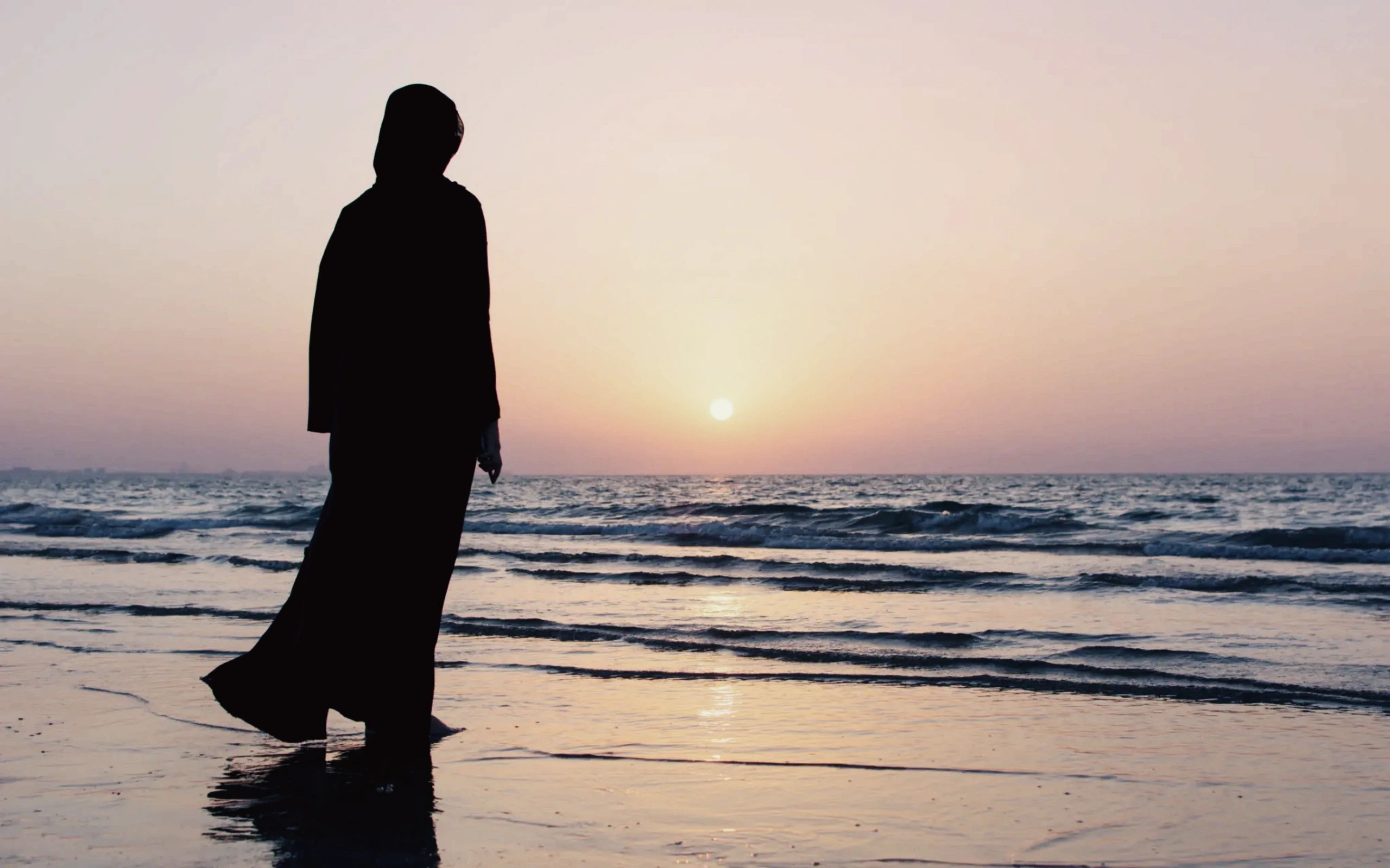 Muslim woman looking upon the sunset in the ocean