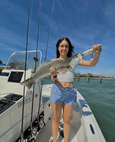 Woman proudly holding a large spotted fish on a boat under clear blue skies.