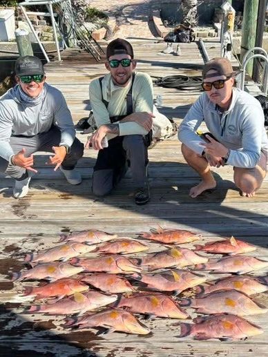 Three men posing with a large catch of fish on a dock.