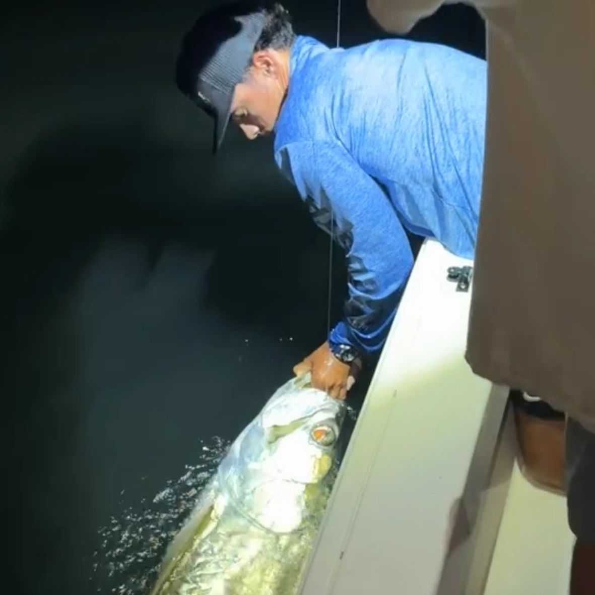 Man releasing a large fish back into the water at night.