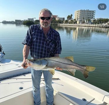 Man holding a large fish on a boat near waterfront buildings.