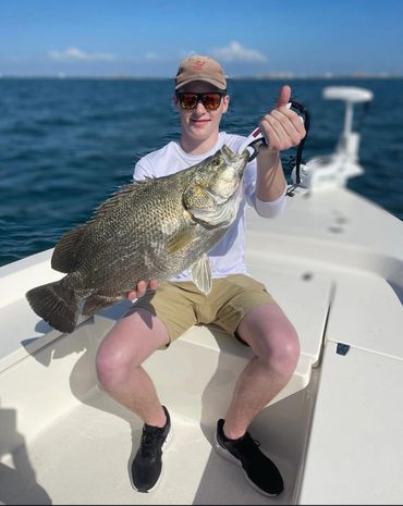 Young man proudly holding a large fish on a boat under clear skies.
