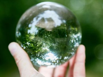 Hand holding a glass sphere reflecting a green outdoor scene.