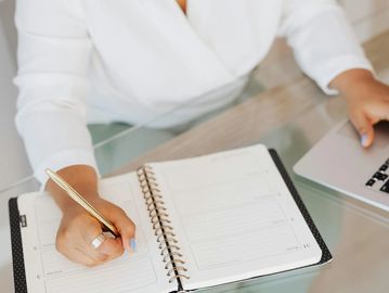Person writing in a planner with a laptop nearby.