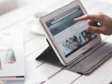 Person using a white tablet on a white wooden table.