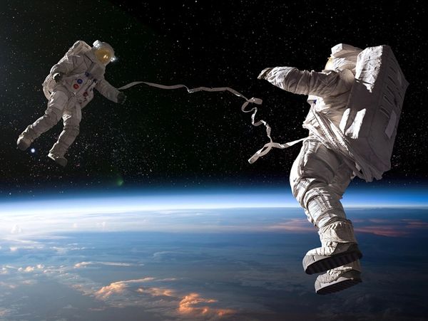Two astronauts tethered together floating above Earth in space.