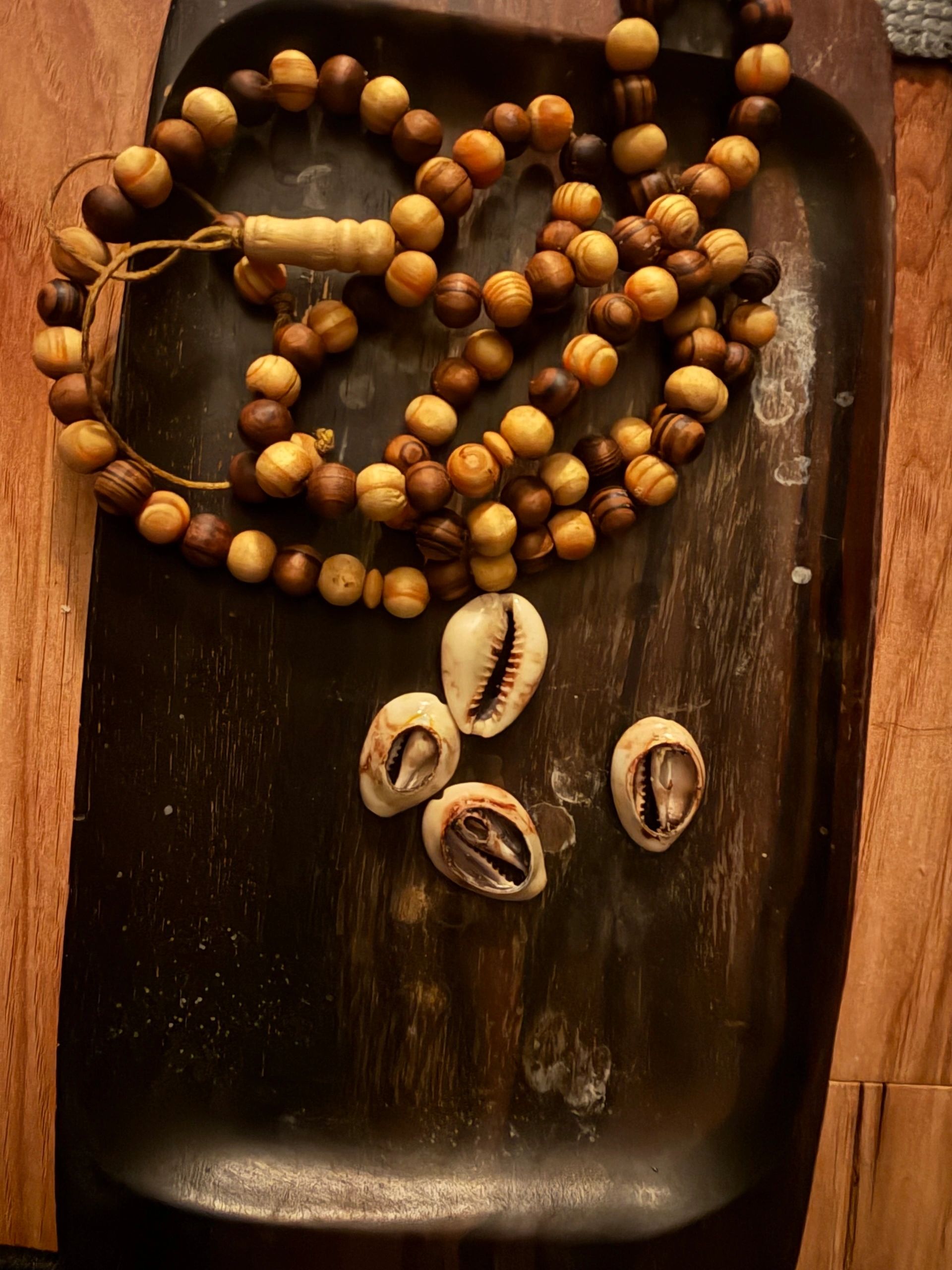 Wooden bead necklace with seashells on a dark wooden tray.