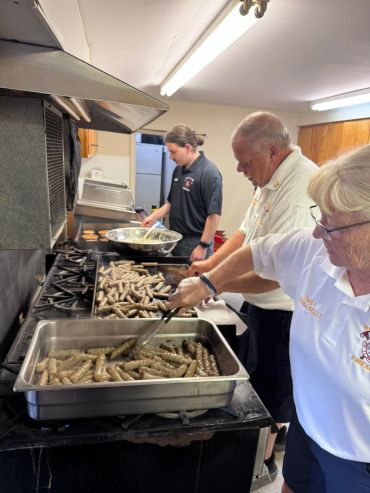 People cooking sausages in a kitchen.