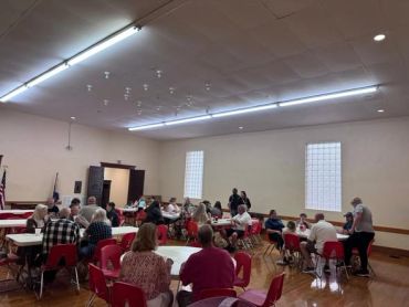 Community gathering with people seated around tables.