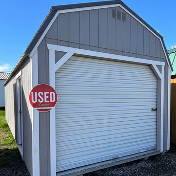 Gray and white used storage shed with a roll-up door.