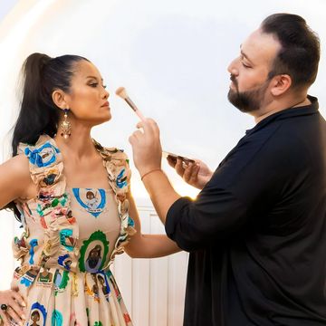 A makeup artist applies makeup to a woman in a colorful dress.