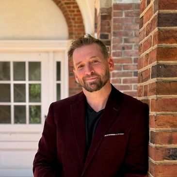 Man with beard leaning against a brick wall.