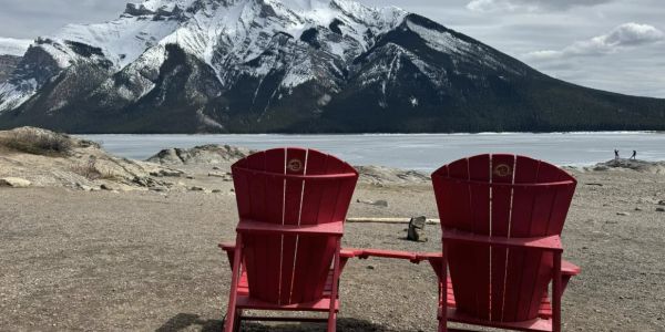 Two red chairs facing snowy mountain and lake.