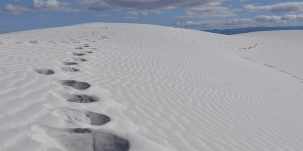 Footprints on pristine white sand dunes under a cloudy sky.