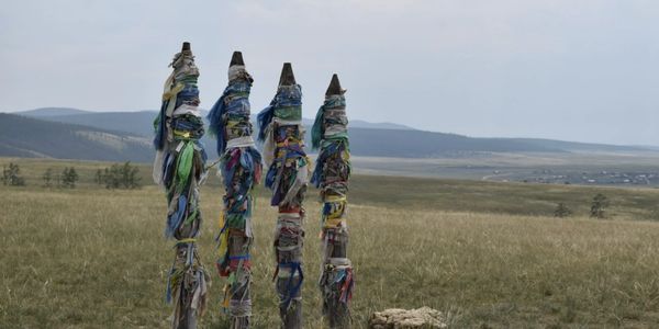 Four tall wooden poles wrapped with colorful cloth in a field.