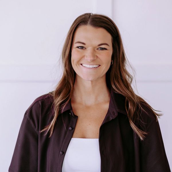 Smiling woman with long brown hair wearing a dark shirt and white top.