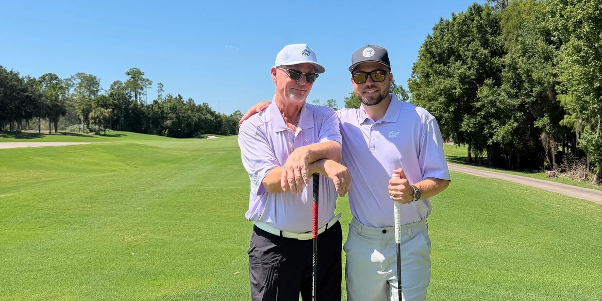 Two men posing with golf clubs on a sunny golf course.