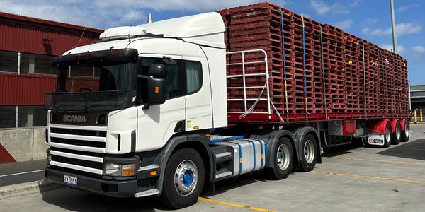 White Scania truck carrying red pallets on a trailer in an industrial area.