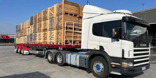 White Scania truck carrying large wooden crates on a trailer.