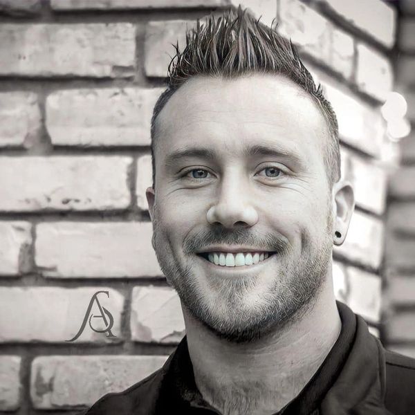 Smiling man with spiked hair against a brick wall.
