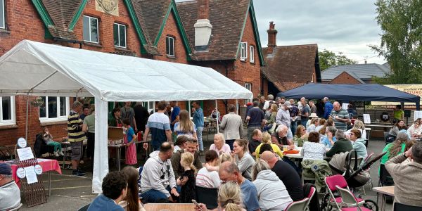 Community gathering with food stalls and seating outside traditional brick buildings.