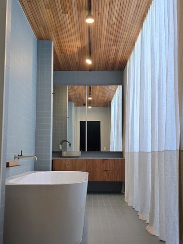 Modern bathroom with wood ceiling, freestanding tub, and large curtain.