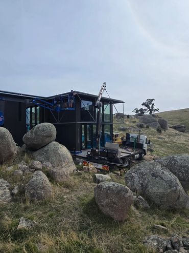 Construction of a modern building in a rocky, grassy landscape.