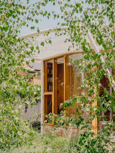 A cozy wooden garden shed with large windows surrounded by greenery.