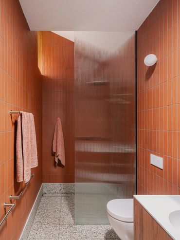 Modern bathroom with terracotta tiles and frosted glass shower partition.