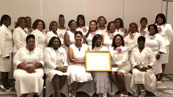 Group of women dressed in white holding a framed certificate.