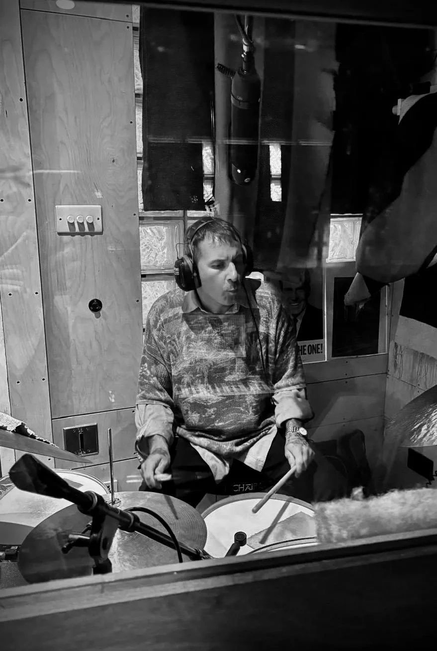 Man playing drums in a recording studio, wearing headphones.