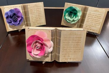 Three wooden book-shaped plaques with colorful paper roses and engraved text.