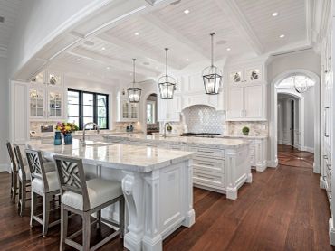 Elegant white kitchen with marble countertops and wooden floor.