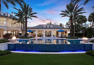Luxury house with pool and palm trees at sunset.