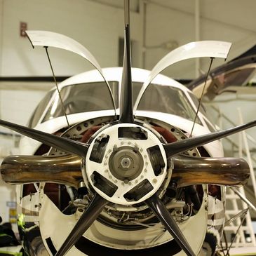 Close-up of a propeller airplane engine with open panels in a hangar.
