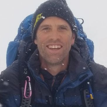 Man smiling outdoors in snowy weather wearing hiking gear.