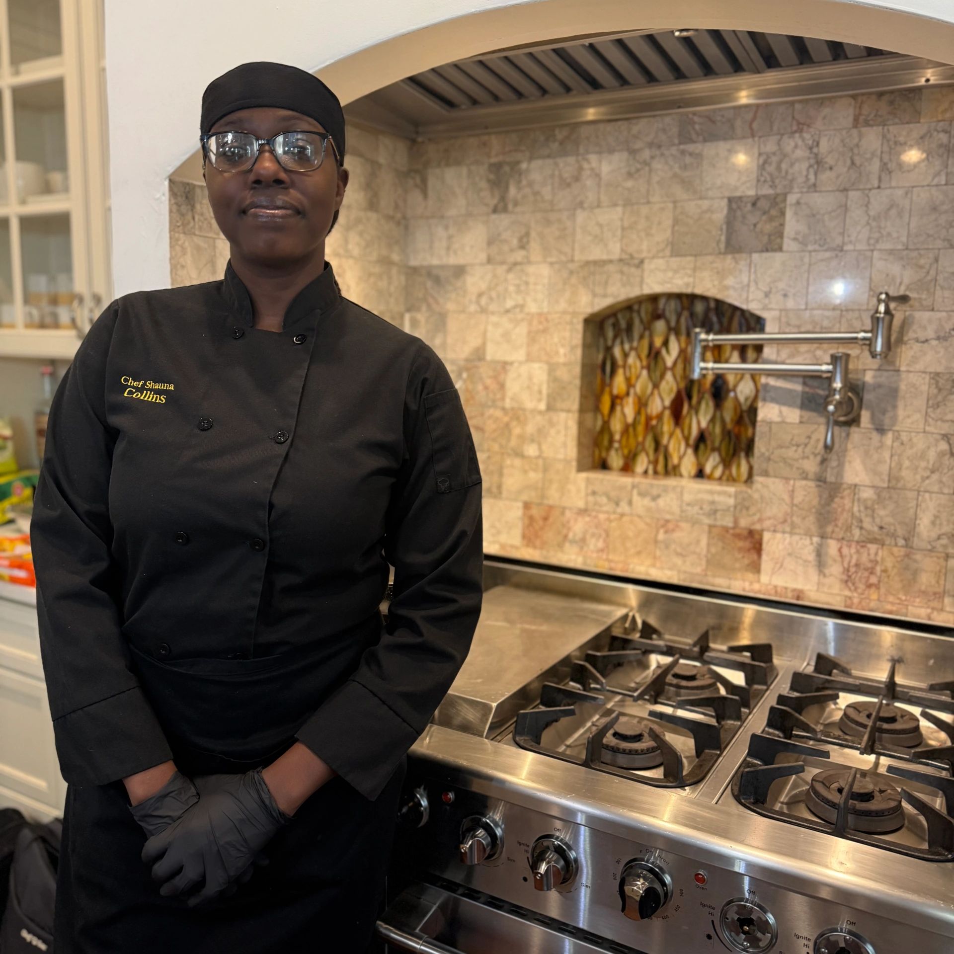 Chef Shauna Collins stands confidently in a kitchen with a large stove behind her.