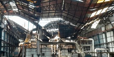Inside a large, aged industrial factory with damaged roof panels.