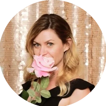 A girl posing for a photo at a party, holding a rose in front of her mouth.